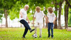 Grandfather and kids play football in sunny park.