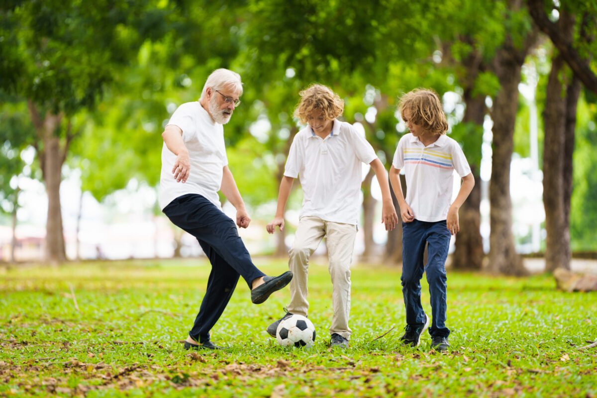 Grandfather and kids play football in sunny park.